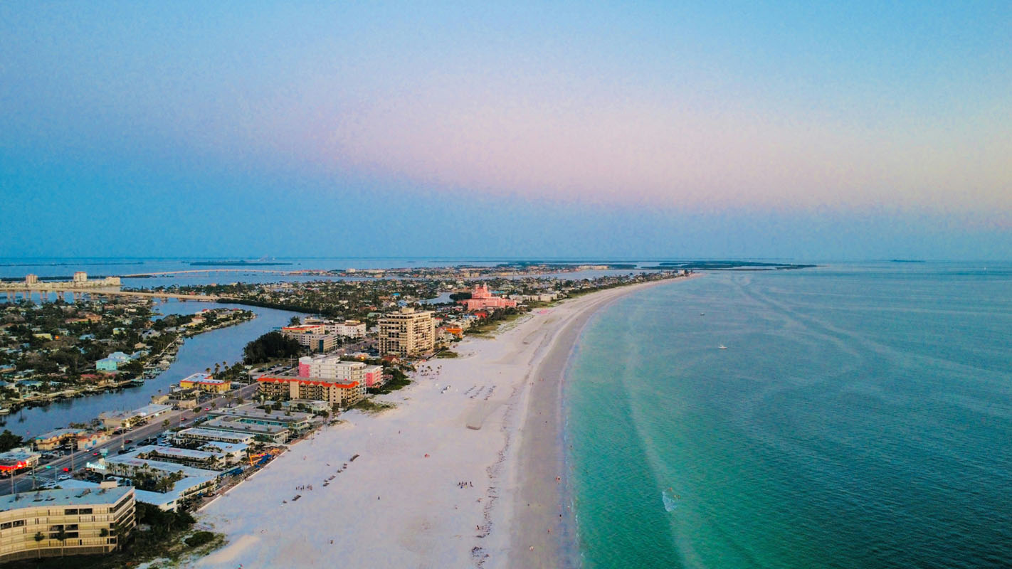 Wide aerial view of turquoise Gulf waters and white sand beach in St. Petersburg Florida at sunset.