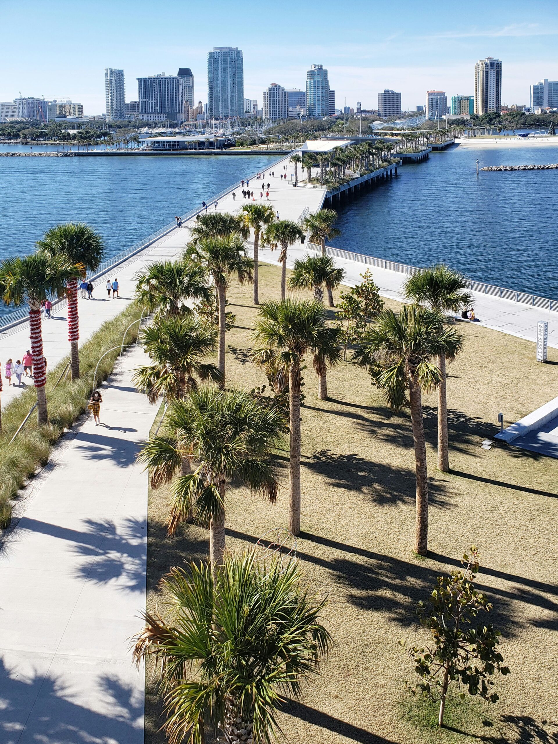 Aerial view of St. Pete Pier walkway lined with palm trees overlooking the water toward the downtown St. Petersburg skyline.