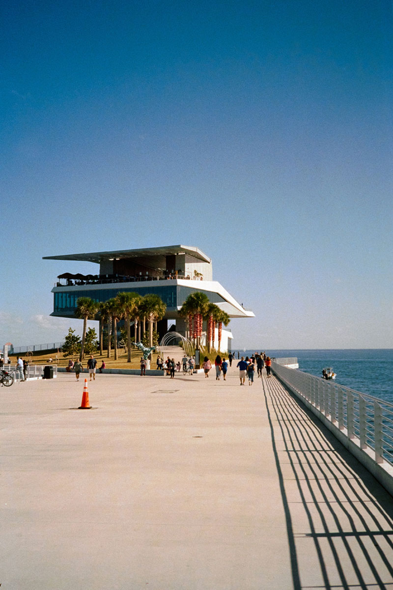Modern architecture of St. Pete Pier with palm trees and visitors walking along the waterfront under a clear blue sky.